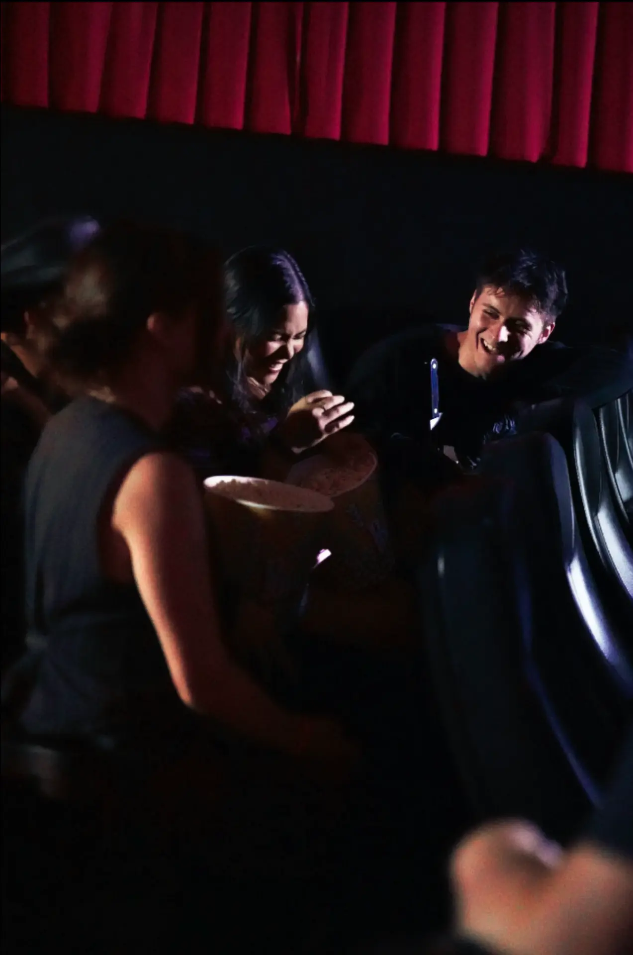 Guests laughing together in the theater seats, sharing a tub of popcorn